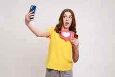 遵循博客肖像惊讶博主青少年女孩黄色的t恤持有社会媒体心按钮使自拍转播画面
