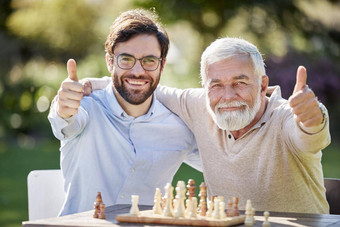 国际象棋生活生活拍摄年轻的高级男人。玩国际象棋显示拇指在户外