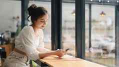 年轻的女人坐着现代咖啡商店聊天在线社会网络聪明的电话