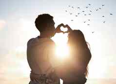 爱使世界美丽的年轻的夫妇使心形状手日落