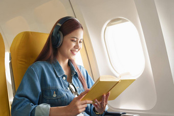 有吸引力的肖像亚洲女人坐着窗口座位经济类阅读书听仪器音乐飞机飞行旅行概念假期放松