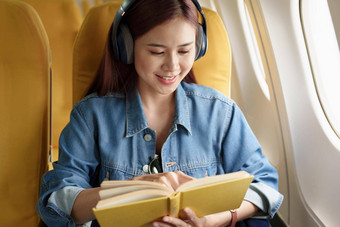 有吸引力的肖像亚洲女人坐着窗口座位经济类阅读书听仪器音乐飞机飞行旅行概念假期放松