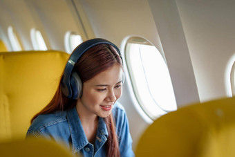 有吸引力的肖像亚洲女人坐着窗口座位经济类听音乐飞行飞机旅行概念假期放松