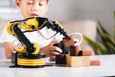 快乐亚洲孩子男孩远程控制玩机器人机手臂选择木块