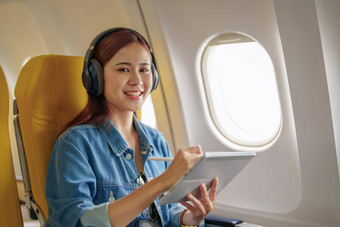 有吸引力的肖像亚洲女人坐着窗口座位经济类平板电脑听仪器音乐飞机飞行旅行概念假期放松