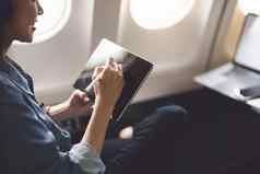 亚洲女人坐着窗口座位经济类平板电脑听仪器音乐飞机飞行旅行概念假期放松