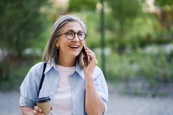 欧洲灰色的头发的女商人会说话的电话<strong>饮料</strong>咖啡<strong>纸杯</strong>城市花园公园成熟的女人咖啡打破穿蓝色的衬衫白色t恤