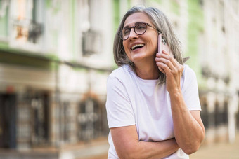 迷人的成熟的业务女人灰色头发会说话的电话持有智能手机站在户外街道城市城市穿白色t恤银头发女人在户外