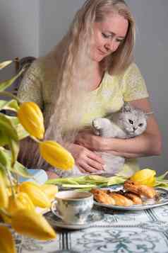 金发女郎中年拥抱小猫喝茶黄色的郁金香书