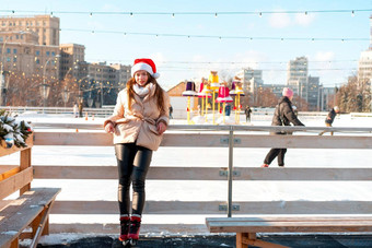 美丽的可爱的年轻的成人女人褐色头发温暖的冬天夹克站冰滑冰溜冰场背景小镇广场圣诞节情绪生活方式