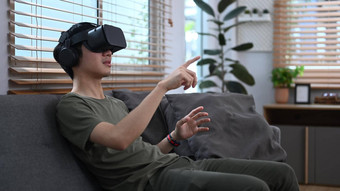 快乐的亚洲男人。玩视频游戏看电影虚拟现实耳机坐着沙发上首页