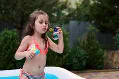 可爱的年女孩时尚的泳衣吹肥皂泡沫充气孩子们池首页花园