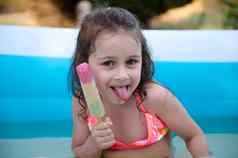 肖像可爱的有趣的女孩摆姿势色彩斑斓的冰奶油坚持户外充气水池