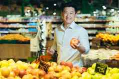 肖像亚洲超市买家男人。选择苹果水果把篮子