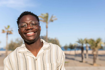 肖像年轻的快乐微笑黑色的男人。穿眼镜在户外背景棕榈树复制空间