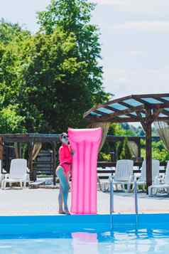 美丽的女人粉红色的泳衣充气床垫站大池夏天假期酒店游泳池年轻的女孩泳衣太阳镜