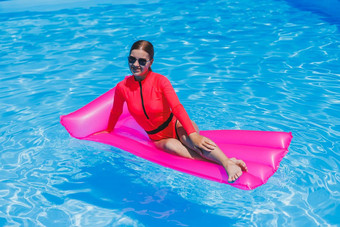 快乐年轻的女人太阳镜粉红色的比基尼浮动充气床垫池夏天假期概念旅行海