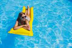 美丽的年轻的女人太阳镜黄色的充气床垫泳衣游泳池奢侈品酒店夏天假期旅行微笑