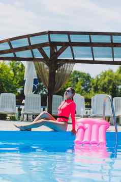 美丽的女人粉红色的泳衣充气床垫站大池夏天假期酒店游泳池年轻的女孩泳衣太阳镜