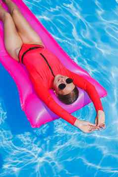 快乐年轻的女人太阳镜粉红色的比基尼浮动充气床垫池夏天假期概念旅行海