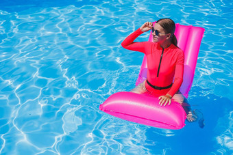 美丽的女孩粉红色的泳衣放松充气粉红色的床垫池纤细的热女人太阳镜泳衣日光浴女人放松奢侈品度假胜地