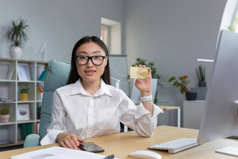 年轻的亚洲女人银行员工持有<strong>信贷</strong>卡手相机微笑