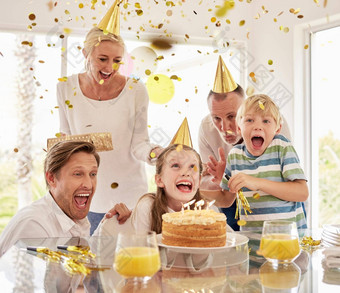 快乐的分代快乐家庭穿聚会，派对帽子庆祝女孩生日五彩纸屑蛋糕首页兴奋孩子们父母祖父母享受特殊的惊喜事件