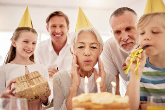 高级女人庆祝生日家庭首页穿聚会，派对帽子吹吹口哨奶奶生日蛋糕快乐的包围孙子丈夫儿子
