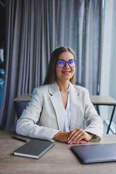 成功的年轻的女经理优雅的休闲夹克光学眼镜坐在办公室工作场所有经验的女人现代移动PC工作办公室