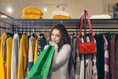 购物狂美丽的年轻的女孩女人服装商店购物中心喜乐购物者礼物站持有绿色纸袋背景衣架衣服包快乐
