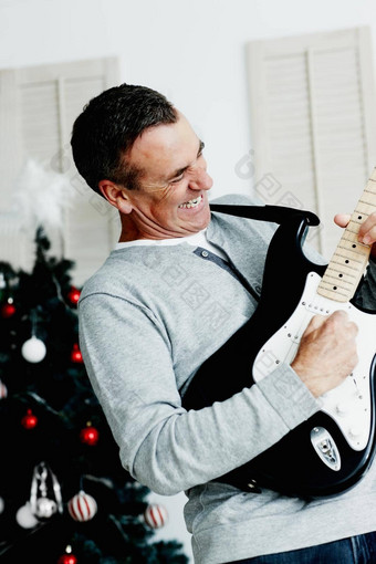 成熟的男人。玩吉他圣诞节树背景肖像精力充沛的成熟的男人。玩吉他圣诞节树背景