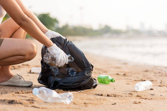 志愿者女人挑选塑料瓶垃圾塑料袋黑色的清洁海滩
