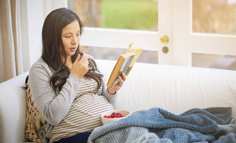 吃健康的重要的有吸引力的年轻的怀孕了女人吃<strong>水果</strong>阅读书放松<strong>沙发</strong>首页