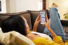特写镜头女人智能手机说谎沙发放松明亮的生活房间年轻的拉美裔女放松发短信手机现代技术首页