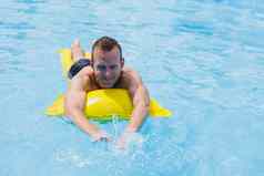 英俊的男人。游泳短裤充气黄色的床垫池夏天假期酒店