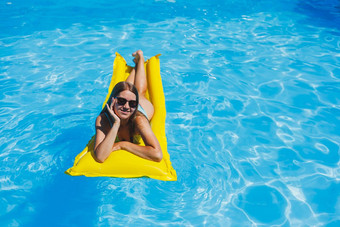 美丽的年轻的女人太阳镜黄色的充气床垫泳衣游泳池奢侈品酒店夏天假期旅行微笑