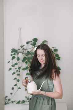 年轻的女人围裙家庭主妇园丁需要护理绿色植物浇水花锅舒适的房间概念园艺爱好