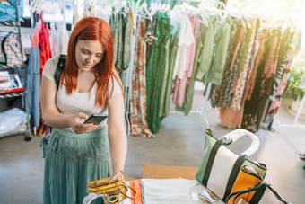 年轻的微笑红色头发的人女孩购物小服装商店采取图片聪明的电话衣服社会网络女孩支出时间购物概念购物