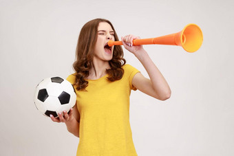 极积极的满意少年女孩黄色的t恤尖叫扩音器持有足球球庆祝胜利最喜欢的足球团队