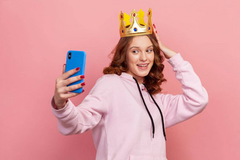 肖像微笑卷曲的头发的十几岁的女孩连帽衫<strong>黄金</strong>皇冠摆姿势智能<strong>手机</strong>相机采取自拍