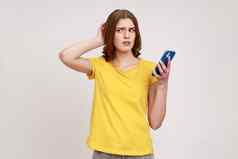 沉思的深思熟虑的青少年女孩黄色的休闲风格t恤站移动电话触碰头怀疑怀疑感觉