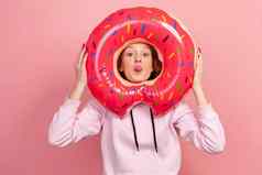 肖像有趣的卷曲的头发的十几岁的女孩连帽衫显示舌头粉红色的甜甜圈橡胶环持有手愚弄休息