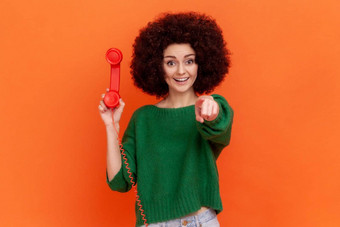 嘿调用微笑友好的<strong>女人</strong>非洲式发型发型穿绿色休闲风格毛衣持有红色的手机指出手指相机