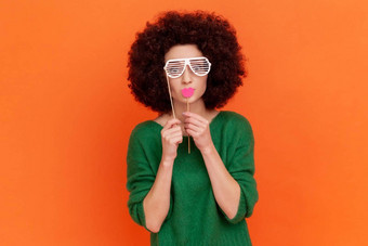 有趣的女人非洲式发型发型穿绿色休闲风格毛衣覆盖眼睛纸眼镜持有红色的嘴唇坚持化妆舞会
