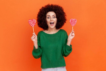 兴奋女人非洲式发型发型绿色休闲风格毛衣持有糖果心形状相机快乐积极的表达式