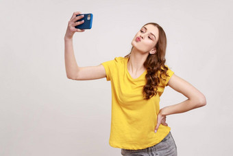 肖像可爱的卷曲的头发的十几岁的女孩黄色的t恤发送吻智能手机相机沟通视频调用流媒体视频博客