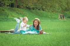 妈妈。阅读书婴儿女孩说谎草公园