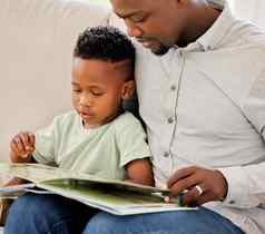 年轻的内容非洲美国父亲阅读书儿子坐着沙发上首页男孩享受故事学习坐着沙发爸爸周末