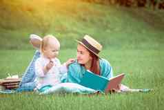 妈妈。阅读书婴儿女孩说谎草公园