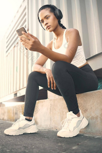适合年轻的拉美裔女人听<strong>音</strong>乐耳机手机采取打破锻炼在户外女运动员发<strong>短信</strong>健身应用程序在线浏览社会媒体看锻炼教程